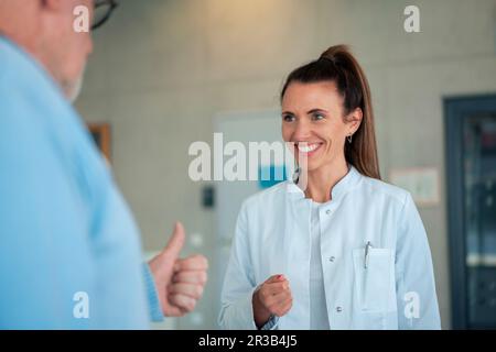 Glücklicher Arzt, der mit Seniorpatienten durch Gesten in der Klinik spricht Stockfoto