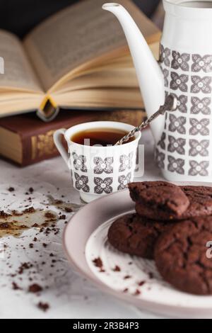 Verschütteter Kaffee auf dem Tisch. Stille Lebenszusammensetzung von Schokoladenkeksen auf dem Teller, Kaffeetasse, C. Stockfoto