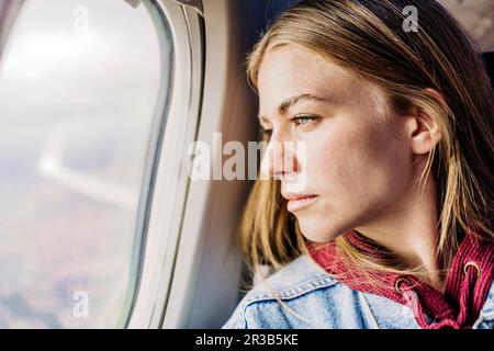 Junge Frau aus Flugzeugfenster Stockfoto