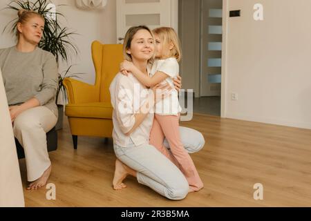 Ein Mädchen flüstert der Mutter ins Ohr und kniet zu Hause Stockfoto