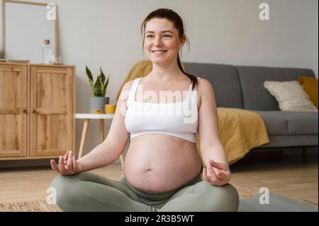 Lächelnde schwangere Frau, die zu Hause Yoga macht Stockfoto