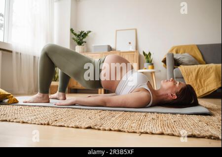 Schwangere Frau, die zu Hause pränatales Yoga auf einer Trainingsmatte macht Stockfoto