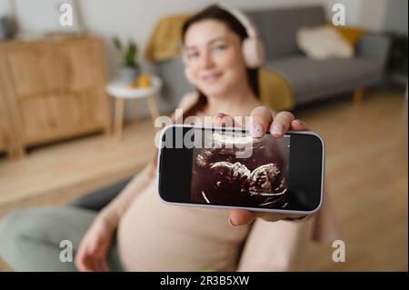 Schwangere Frau zeigt Ultraschallbild auf Smartphone-Bildschirm Stockfoto