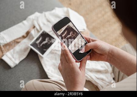 Schwangere Frau macht Ultraschallbild mit Smartphone zu Hause Stockfoto