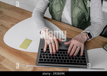 Hände einer Seniorin, die zu Hause online über ein Notebook einkauft Stockfoto