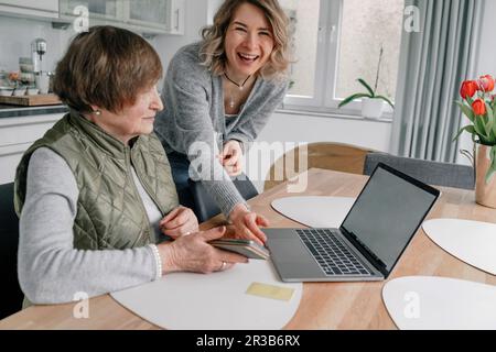 Glückliche Enkelin von Seniorin mit Laptop auf dem Tisch zu Hause Stockfoto