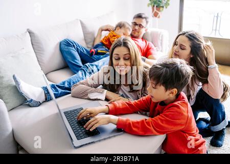 Ein Junge, der ein Notebook von seiner Familie benutzt und zu Hause im Wohnzimmer sitzt Stockfoto