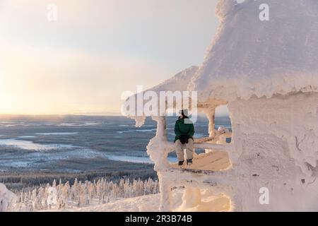 Eine Frau, die im Winter auf der Veranda eines schneebedeckten Hauses sitzt Stockfoto