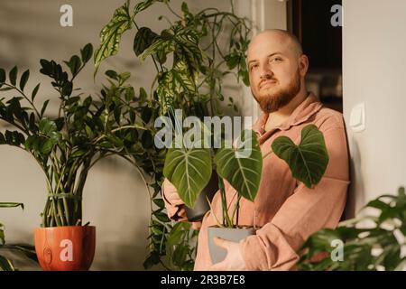 Ein bärtiger Mann, der zu Hause Topfpflanzen hält Stockfoto