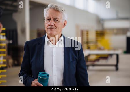 Ein umsichtiger Geschäftsmann, der eine Wasserflasche in der Fabrik hält Stockfoto