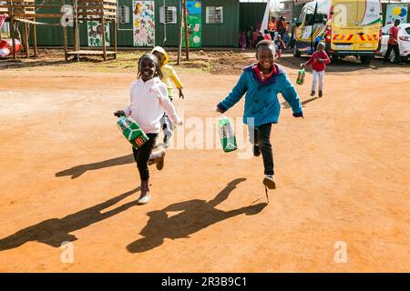 Junge afrikanische Vorschulkinder laufen mit einem Laib Brot auf dem Spielplatz einer Kindergartenschule Stockfoto