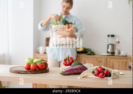 Auswahl an frischem Bio-Gemüse in wiederverwendbaren Beuteln auf dem Tisch mit der Frau zu Hause Stockfoto