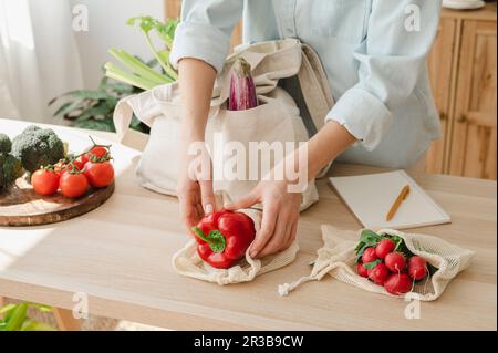 Frau, die zu Hause Gemüse in Mehrwegbeuteln auf dem Tisch hält Stockfoto