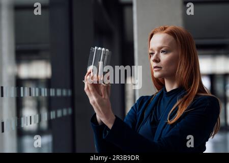 Rothaarige Geschäftsfrau, die Maschinenteile im Büro untersucht Stockfoto