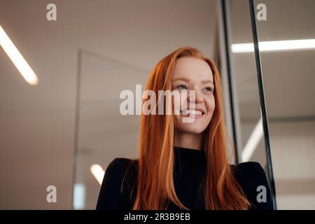 Kontemplative Geschäftsfrau in der Nähe der Wand im Büro Stockfoto