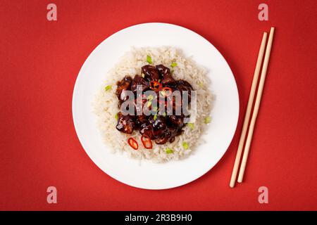 Süßes und saures Fleisch unter Rühren in klebriger Sauce mit Reis auf weißem Teller mit Holzstäbchen, traditionelles chinesisches Gericht Stockfoto