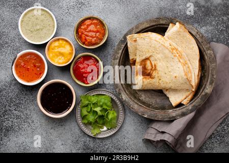 Verschiedene indische Chutneys in rustikalen Schüsseln und Fladenbrot auf grauem Betonhintergrund Stockfoto