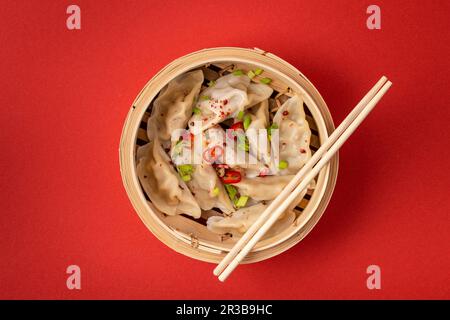 Traditionelle gedämpfte chinesische Knödel in Bambusdampfer mit Holzstäbchen auf rotem Hintergrund, Nahaufnahme, Draufsicht Stockfoto