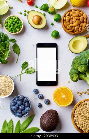 Gemüse, Obst, Linsen und Mandeln um ein Smartphone herum Stockfoto