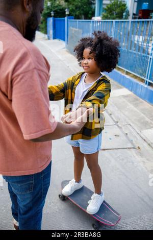 Vater unterstützt Tochter, die auf dem Skateboard steht Stockfoto
