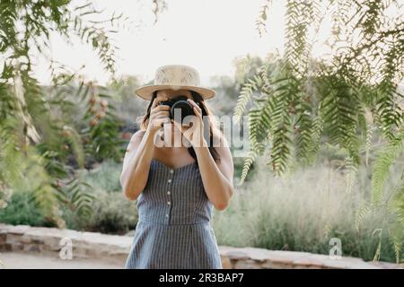 Eine Frau, die mit der Kamera fotografiert, in der Nähe von Pflanzen steht Stockfoto