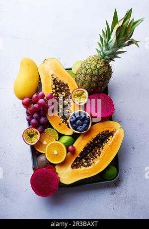 Tropische Früchte liegen flach mit Mango, Papaya, Pitahaya, Passionsfrucht, Trauben, Limetten und Ananas auf einem Tablett Stockfoto