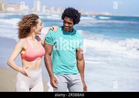 Fröhliches Paar in Sportbekleidung, das am Meer spaziert Stockfoto