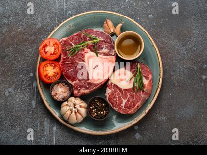 Zutaten für Ossubuco – Rohe Kalbstangen auf dem Teller mit Gewürzen, Tomaten, Kräutern und Olivenöl Stockfoto