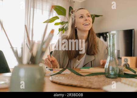 Glückliche junge Frau, die am Tisch malt Stockfoto