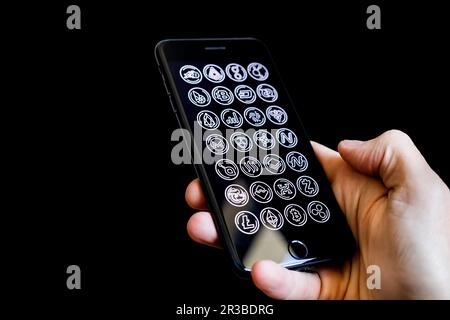 Kaukasische männliche Hand hält ein Mobiltelefon mit Kryptowährungssymbolen auf dem Bildschirm Stockfoto