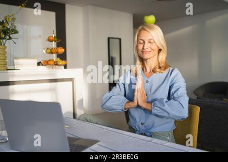 Freiberuflerin meditiert mit geschlossenen Augen und balanciert Apfel auf dem Kopf Stockfoto