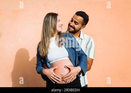 Glückliches Paar mit Händen am Bauch vor der Wand Stockfoto