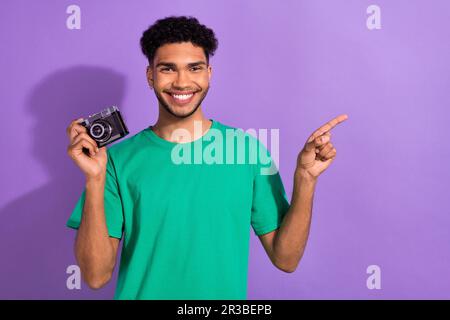 Foto eines positiven coolen Mannes Tragen Sie ein grünes T-Shirt, auf dem der Finger leer ist und der klassische Kamera einen isolierten lilafarbenen Hintergrund zeigt Stockfoto