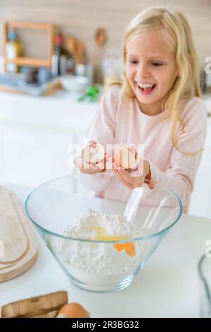 Glückliches Mädchen, das zu Hause Eier in Mehl zerbricht Stockfoto