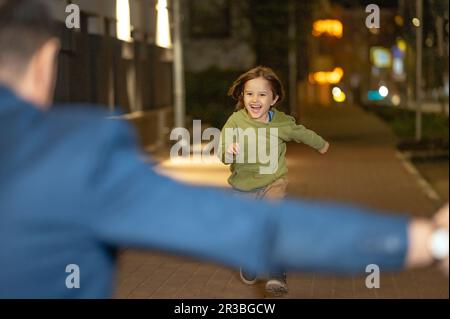 Fröhlicher Sohn, der nachts auf dem Bürgersteig auf den Vater zuläuft Stockfoto