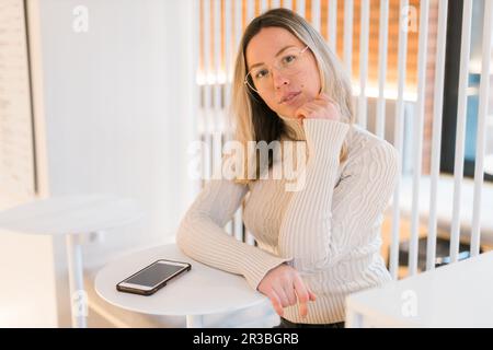 Porträt einer beruhigenden, glücklichen, gemütlichen Frau mit Brille im gestrickten, winterweißen, warmen Pullover im Café Stockfoto