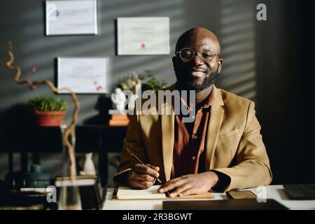 Lächelnder Psychologe mit Blazer am Schreibtisch im Büro Stockfoto