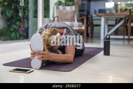 Frau, die zu Hause Janu Sirsasana auf einer Trainingsmatte praktiziert Stockfoto