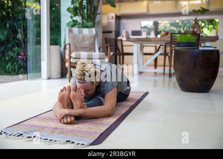 Frau, die zu Hause sitzend vorwärts gebogen 2 auf der Trainingsmatte posiert Stockfoto