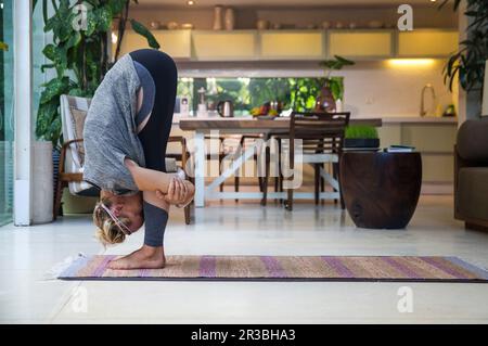 Eine Frau, die zu Hause im Wohnzimmer die große Zeh-Pose praktiziert Stockfoto