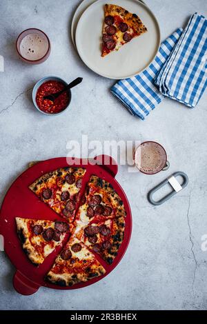 Holzofenpizza mit Peperoni und Fior di Latte, serviert mit Chilisauce und Bier Stockfoto