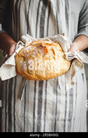 Eine Frau mit Schürze hält frisch gebackenes Brot in der Hand Stockfoto