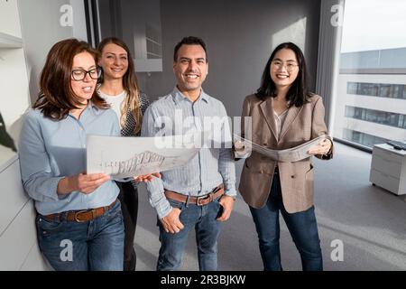 Selbstbewusste Geschäftsleute, die im Büro stehen und Architekturpläne haben Stockfoto