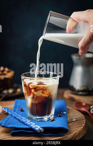 Eiskalter Kaffee mit einer Hand, die Milch eingießt Stockfoto