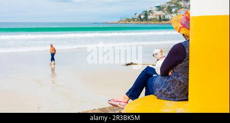 Eine Frau am Strand mit einem Hund auf dem Schoß Stockfoto