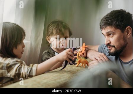 Söhne, die zu Hause mit Spielzeug-Dinosauriern spielen Stockfoto