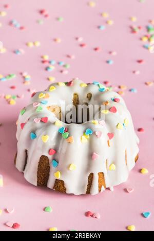 Bundt-Kuchen mit weißer Glasur und farbenfrohen herzförmigen Zuckerstreuseln zum Valentinstag Stockfoto