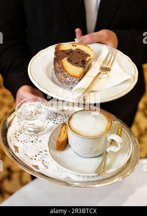 Eine Kellnerin serviert Kaffee und ein Stück Kuchen Stockfoto