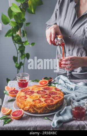 Blut-Orange-Kuchen auf dem Kopf und eine Frau, die Saft eingießt Stockfoto