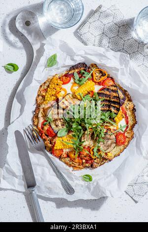 Kohlenhydratarme Pizza auf Blumenkohlbasis, Mozzarella-Käse, Tomaten, Aubergine, Paprika, Mais- und Raketensalat Stockfoto